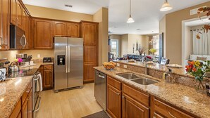 A modern kitchen with granite countertops, stainless steel appliances, and wooden cabinets. - Top Floor 2000 sq ft Lakefront Corner Condo | Walk to Epic (Orlando)