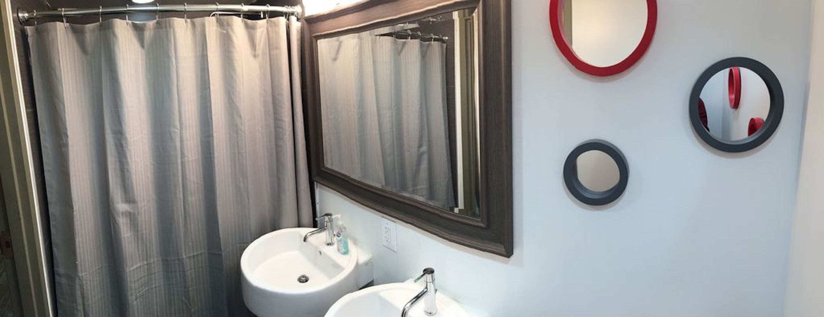 Une salle de bain avec un rideau de douche, un lavabo, un miroir et deux miroirs fixés au mur.