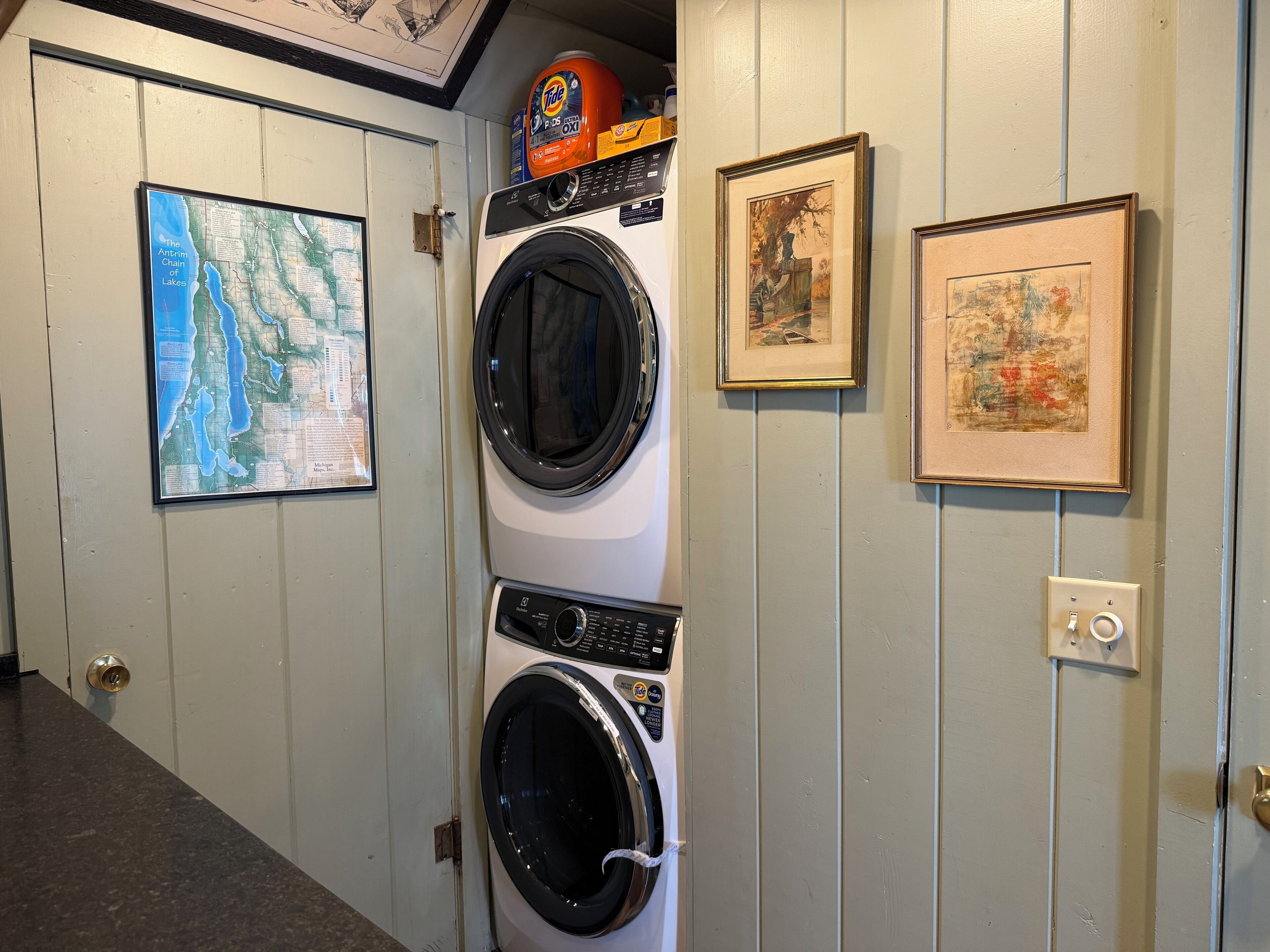 A laundry area with a washing machine, a map on the wall, and two framed pictures.