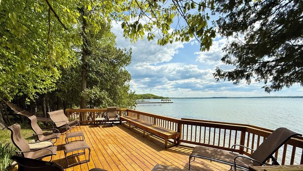 Una terraza de madera con mobiliario exterior, con vista a un lago.