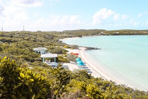 Une plage bordée d’une eau turquoise et limpide, entourée d’une végétation luxuriante et de quelques bâtiments.