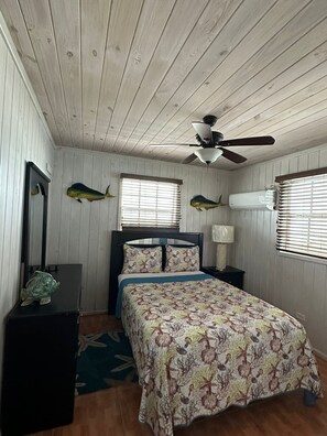 Une chambre à coucher comprenant un lit, un ventilateur de plafond, une table de chevet, une lampe et deux décorations murales représentant des poissons.