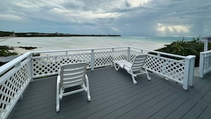 A deck with two white chairs overlooking a beach with boats and a cloudy sky. - Seashell Cottage with breathtaking views! Near Swimming Pigs.  (exuma)