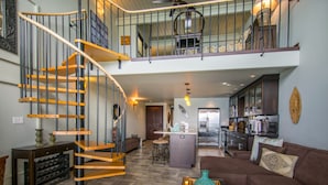 A spacious living area with a wooden spiral staircase, a brown sofa, and a kitchen in the background.