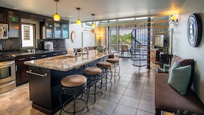 A modern kitchen with a central island, bar stools, and a staircase leading to a balcony.