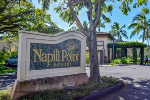 Une enseigne indiquant l’emplacement du Napili Point Resort, offrant une vue dégagée sur la végétation environnante et sur un bâtiment situé au loin.