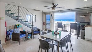 A modern interior with a dining area, kitchen, and a staircase leading to a balcony with a view of the ocean.