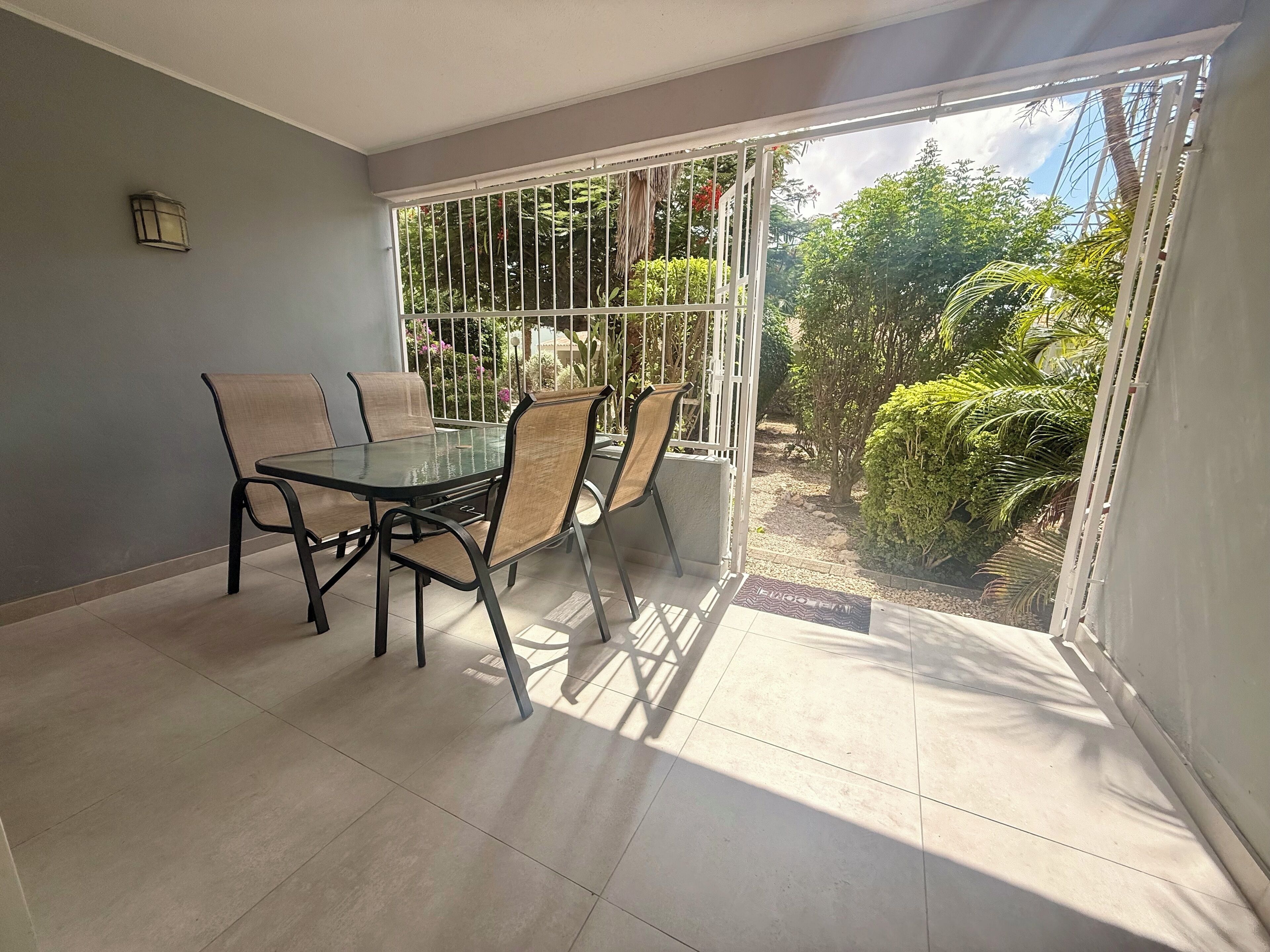 Un balcón con puerta de cristal, una mesa con sillas y vista a follaje.