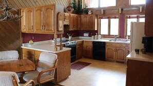 Cozinha com armários de madeira, área de jantar com mesa e cadeiras, e janela que traz luz natural.