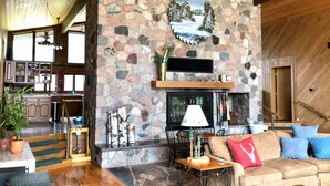 Uma sala de estar aconchegante com lareira de pedra, móveis de madeira e vista para a cozinha.