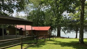 A lakeside cabin with a red roof, surrounded by a wooden deck and a grassy area. - Beautiful Rustic Cabin On Lincoln Lake Is A Sportsman paradise.   (Kelso)