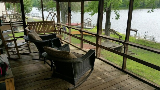 A covered outdoor seating area with wicker chairs and a swing set, overlooking a lake. - Beautiful Rustic Cabin On Lincoln Lake Is A Sportsman paradise.   (Kelso)