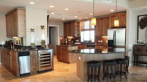 A modern kitchen with wooden cabinets, a central island with stools, and a stainless steel refrigerator. - 360° View of Water - The Entire 18th Floor - 4 Bedroom Penthouse (Gulf Shores)