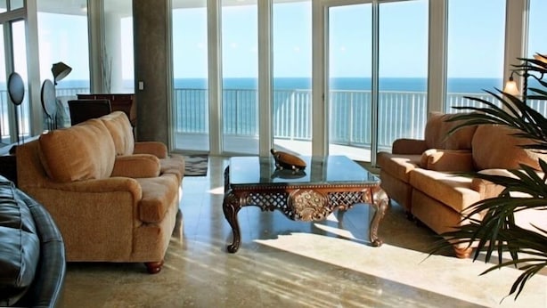 A spacious living area with a large glass wall offering a view of the ocean. - 360° View of Water - The Entire 18th Floor - 4 Bedroom Penthouse (Gulf Shores)