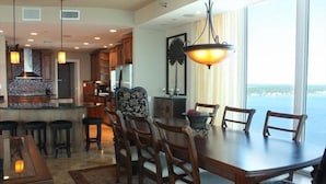 A dining area with a large table and chairs, a bar area with stools, and a view of the ocean. - 360° View of Water - The Entire 18th Floor - 4 Bedroom Penthouse (Gulf Shores)