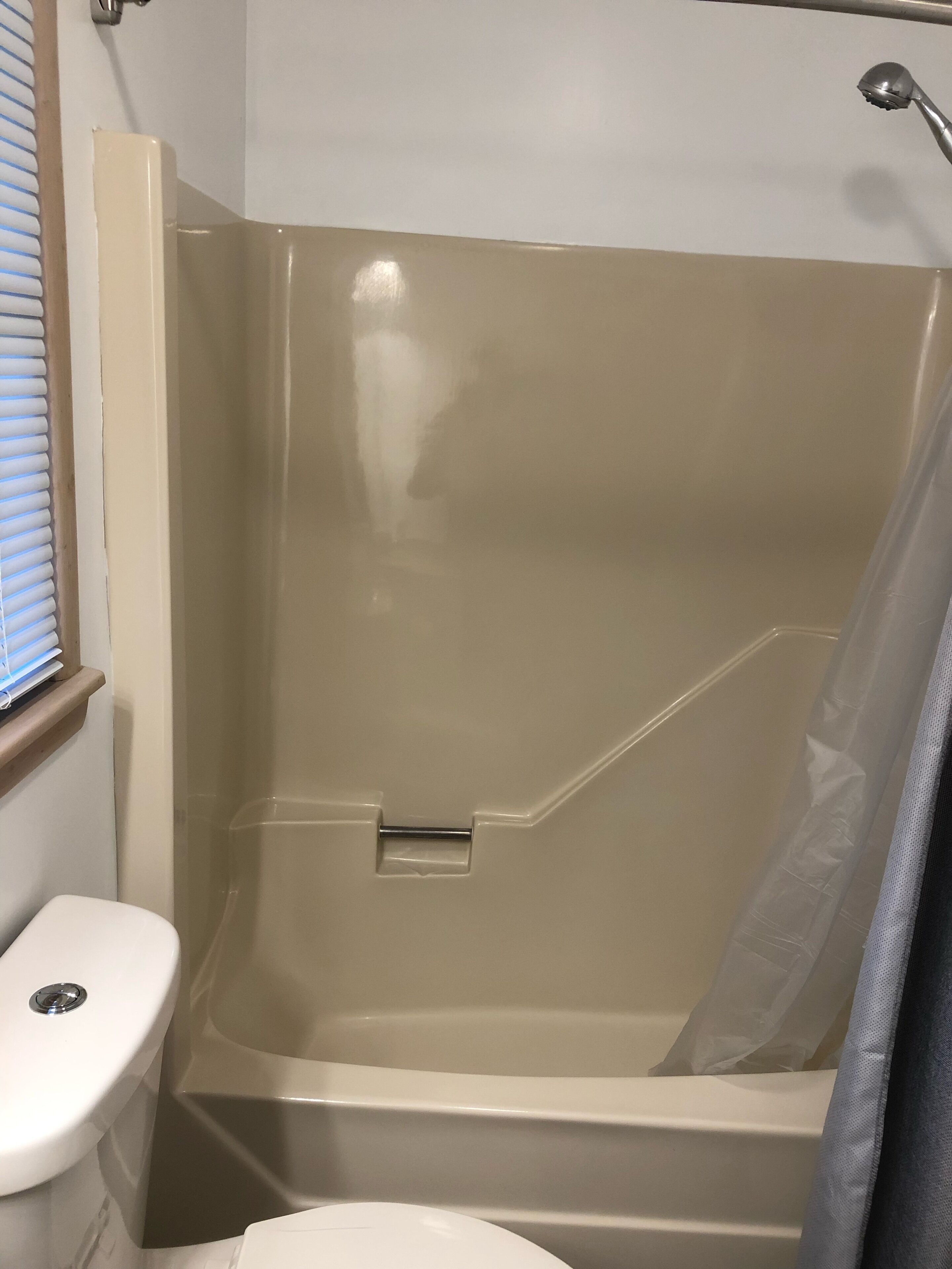 A shower with a glass door, a white toilet, and a window with blinds.