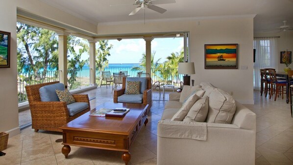 A spacious living room with a view of the ocean, a balcony with wicker furniture, and a dining area. - Villa Renaissance 201: Book August Now And Save 10%! (Providenciales)