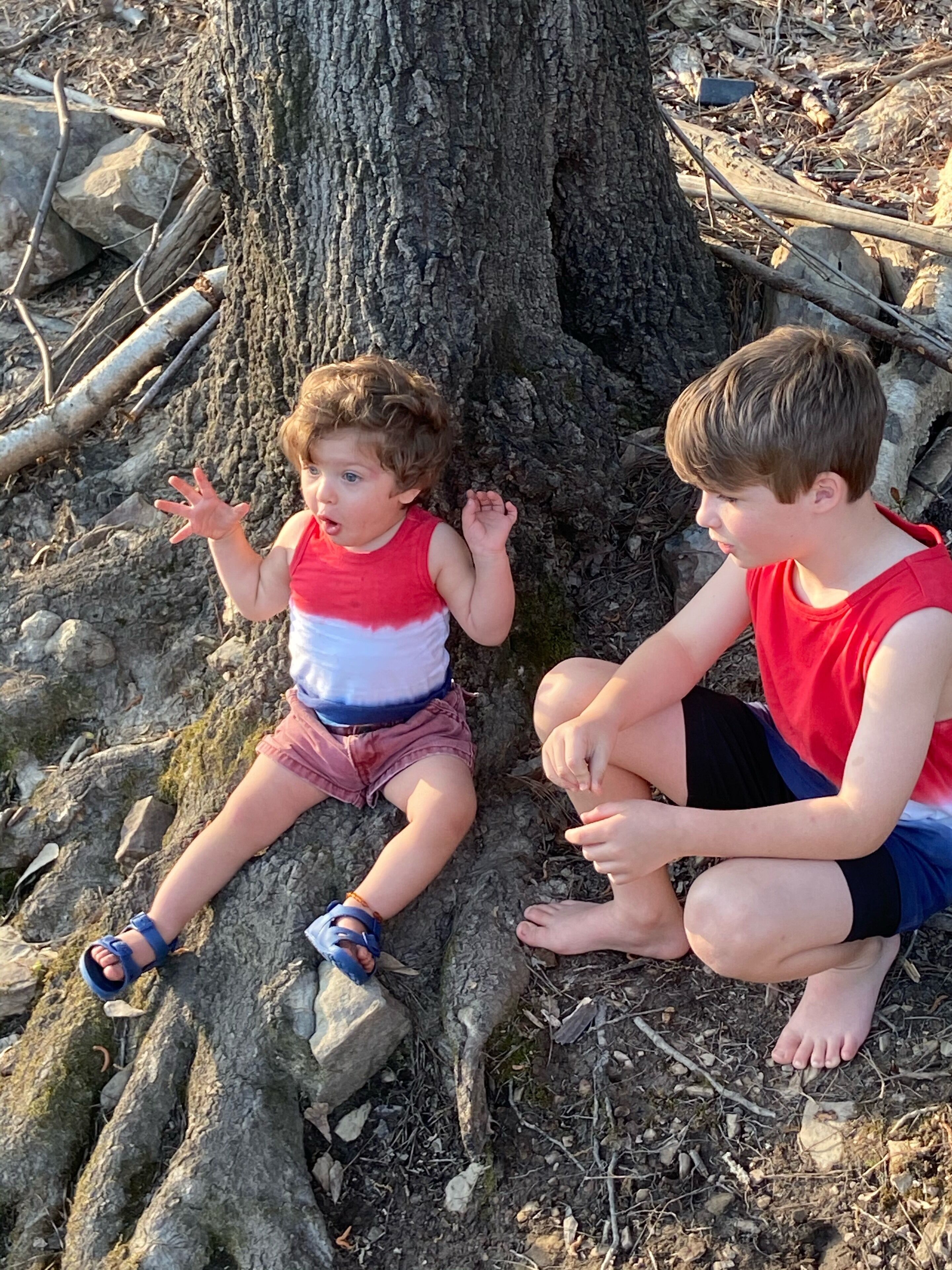 Dos niños sentados sobre una raíz de árbol.