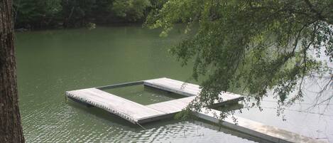 A wooden dock extending into a calm body of water, surrounded by dense greenery.