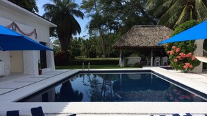 A swimming pool with lounge chairs and umbrellas, surrounded by palm trees and a thatched-roof structure. - Golf (in Front Tee 11), Pool, Service, One Story, 4 Rooms, Internet, Palapa, Van (Ixtapa, Zihuatanejo)