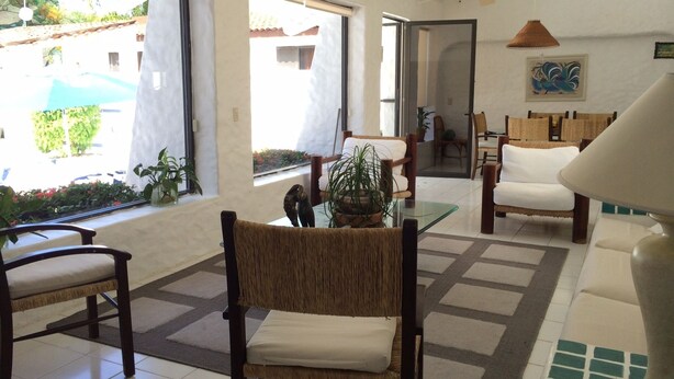 A spacious living area with a large window, a ceiling fan, and a dining area with chairs and a table. - Golf (in Front Tee 11), Pool, Service, One Story, 4 Rooms, Internet, Palapa, Van (Ixtapa, Zihuatanejo)