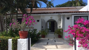 A building with a white facade, a tiled roof, and a central entrance with a metal gate. - Golf (in Front Tee 11), Pool, Service, One Story, 4 Rooms, Internet, Palapa, Van (Ixtapa, Zihuatanejo)