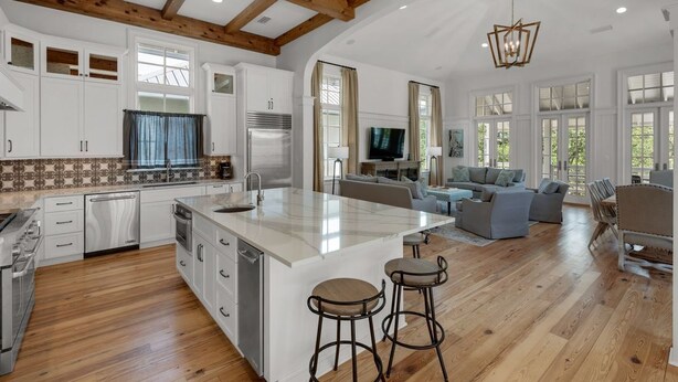 A spacious kitchen with wooden beams, a large island with stools, white cabinetry, and a dining area with a sofa and TV. - PRIVATE BEACH ACCESS-Newly Refurbished-Pool-4 Bikes-Close to Town Center/Beach (Panama City Beach)