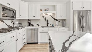 A modern kitchen with white cabinetry, a stainless steel refrigerator, and a marble countertop. - Spacious, newly remodeled home near I-35 in Edmond (Edmond)