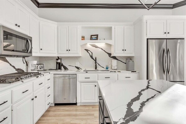 A modern kitchen with white cabinetry, a stainless steel refrigerator, and a marble countertop. - Spacious, newly remodeled home near I-35 in Edmond (Edmond)