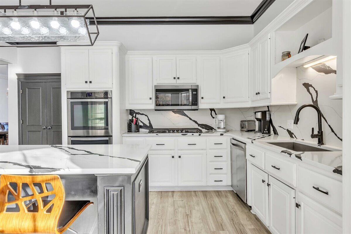 A modern kitchen with white cabinetry, a central island, a microwave, and a sink.