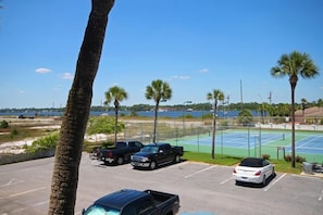 Guests can enjoy a scenic view of the nearby water from the tennis court, surrounded by lush greenery and a secure fence.