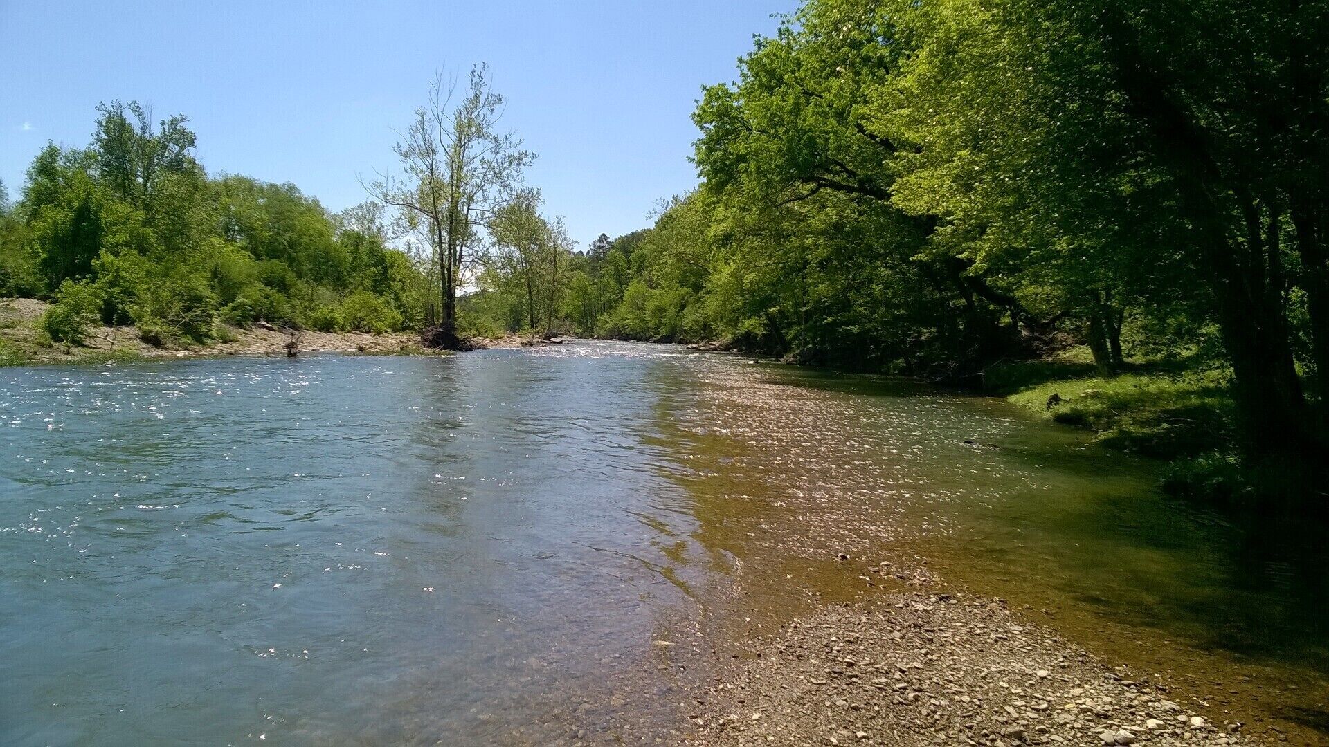 Une rivière aux eaux claires, bordée d’arbres et dont les rives sont rocheuses.