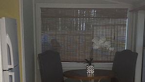 A compact kitchen with a dining table, two chairs, a refrigerator, and a window with blinds.
