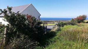 Ein weißes Gebäude mit geneigtem Dach, umgeben von Grün und Blick aufs Meer.
