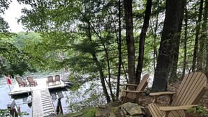 A lakeside deck with wooden chairs, a dock, and a stone pathway. - Spa Cabin: Lakefront w Private Sauna & Hot Tub, Kayaks, Dock, 5 Star Clean Rated (Oakland)