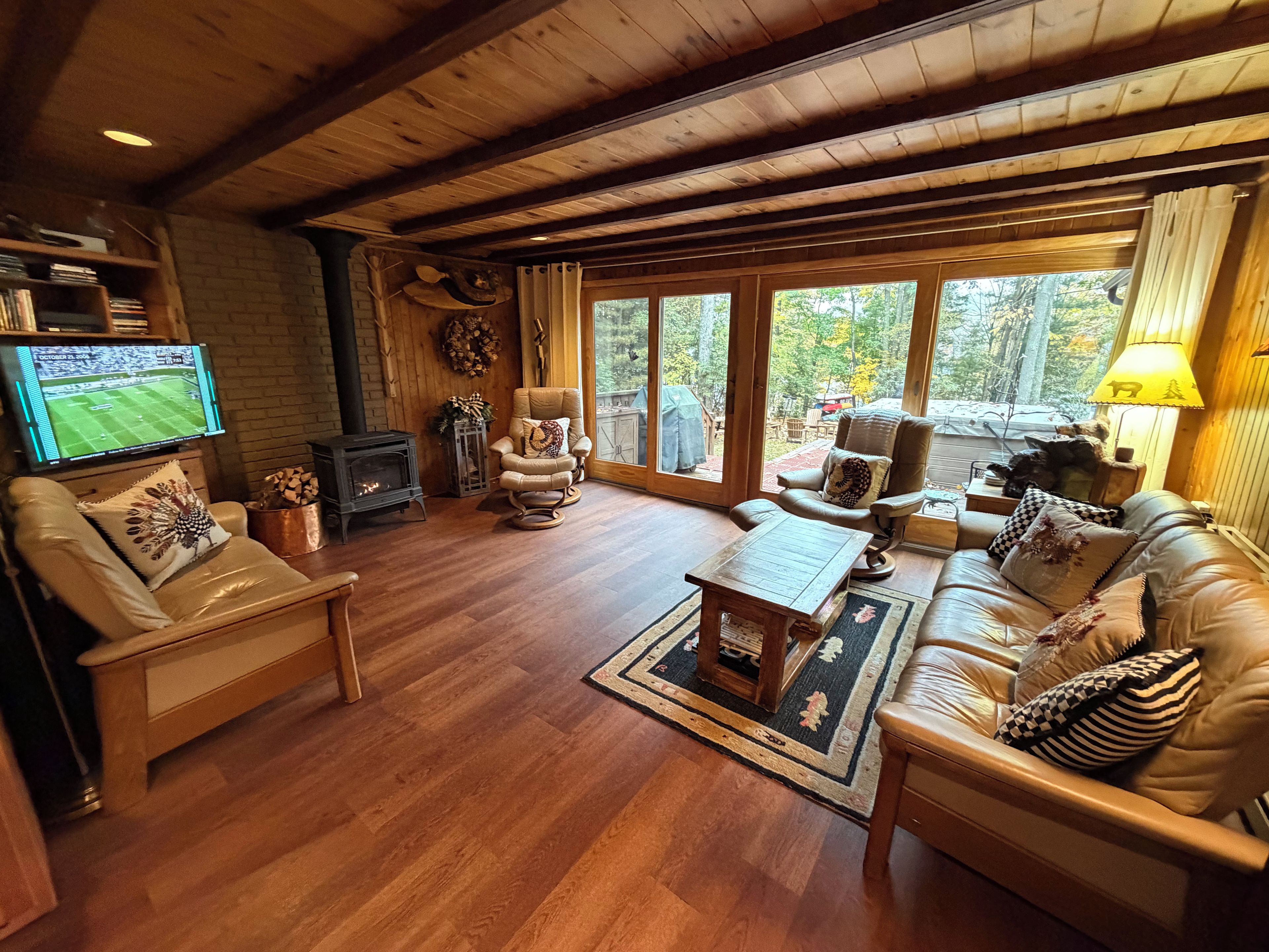 A cozy living room with a fireplace, leather sofas, a television, and a large window with a view of trees.