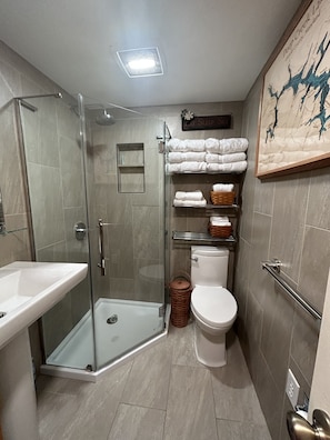 A modern bathroom with a glass shower enclosure, a white sink, a toilet, and a towel rack with neatly folded towels.