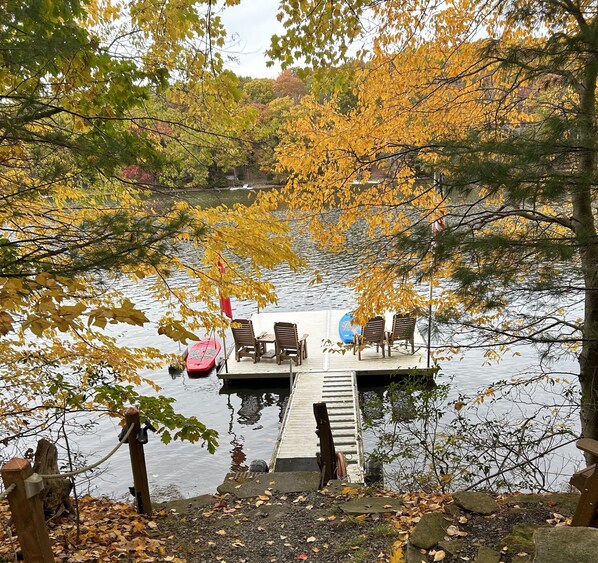 A dock with chairs and a red boat, surrounded by autumn foliage.