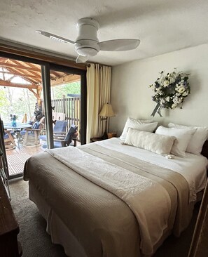 A bedroom with a bed, a ceiling fan, a window with curtains, and a wall-mounted flower arrangement.