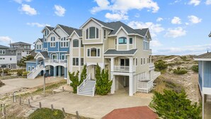 A multi-story residential building with a prominent front porch, multiple windows, and a well-maintained lawn. - Luxurious Oceanfront Home with Private Pool, Hot Tub, Elevator, Tiki Bar (Avon)