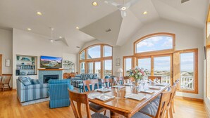 A spacious living room with a large wooden dining table, blue upholstered sofas, and a fireplace. - Luxurious Oceanfront Home with Private Pool, Hot Tub, Elevator, Tiki Bar (Avon)