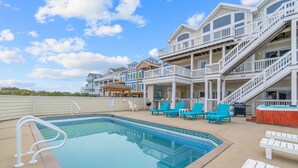 A pool area with a clear blue pool, white lounge chairs, and a covered seating area. - Luxurious Oceanfront Home with Private Pool, Hot Tub, Elevator, Tiki Bar (Avon)