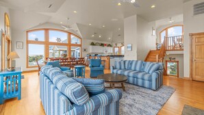 A spacious living room with striped sofas and a dining area with wooden chairs. - Luxurious Oceanfront Home with Private Pool, Hot Tub, Elevator, Tiki Bar (Avon)