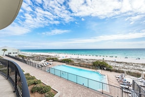 Ein Pool mit Blick auf Strand und Meer, Liegestühle und ein Gebäude mit weißer Fassade.
