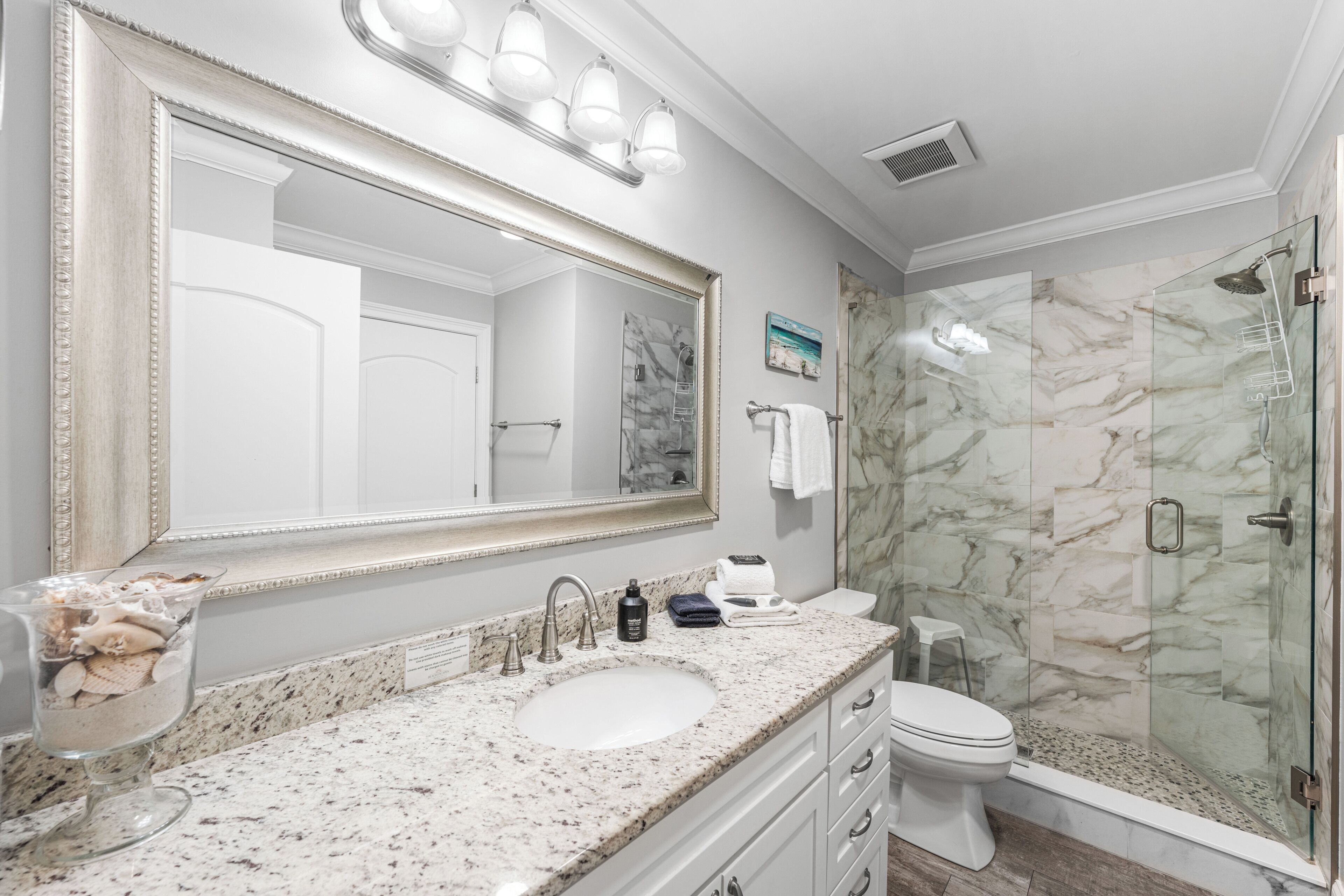 Une salle de bain avec un grand miroir, un lavabo, des toilettes et une douche à parois de verre.