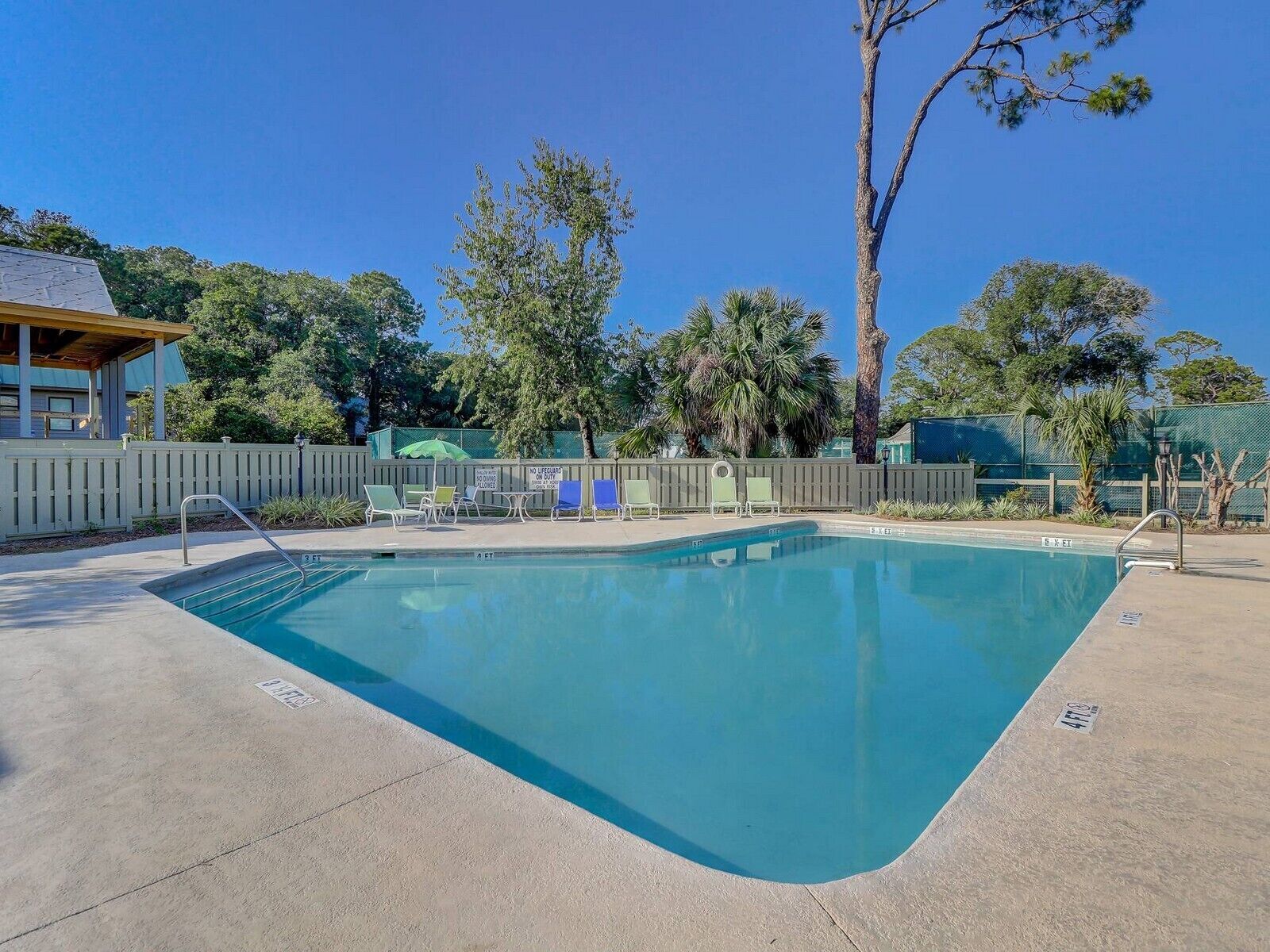 A swimming pool with a wooden deck, lounge chairs, and a fence.