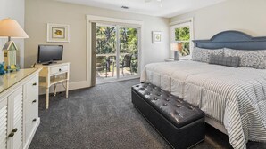 Ein Schlafzimmer mit Bett, Schreibtisch, Fernseher, Deckenventilator und Blick durch eine Glastür.