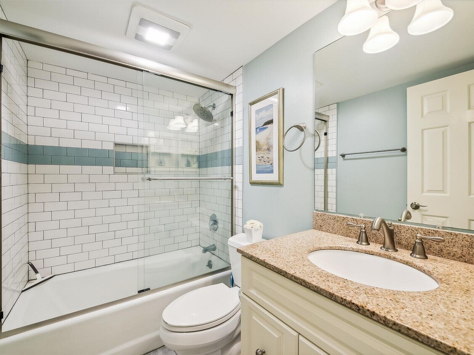 A bathroom with a glass-enclosed shower, a white toilet, a sink with a granite countertop, and a mirror above the sink.