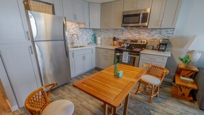 Una cocina moderna con armarios de colores claros, un refrigerador de acero inoxidable, un microondas y una mesa de comedor de madera con dos sillas de mimbre.