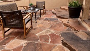 Une terrasse extérieure avec un sol en pierre, des meubles en osier et une plante en pot.